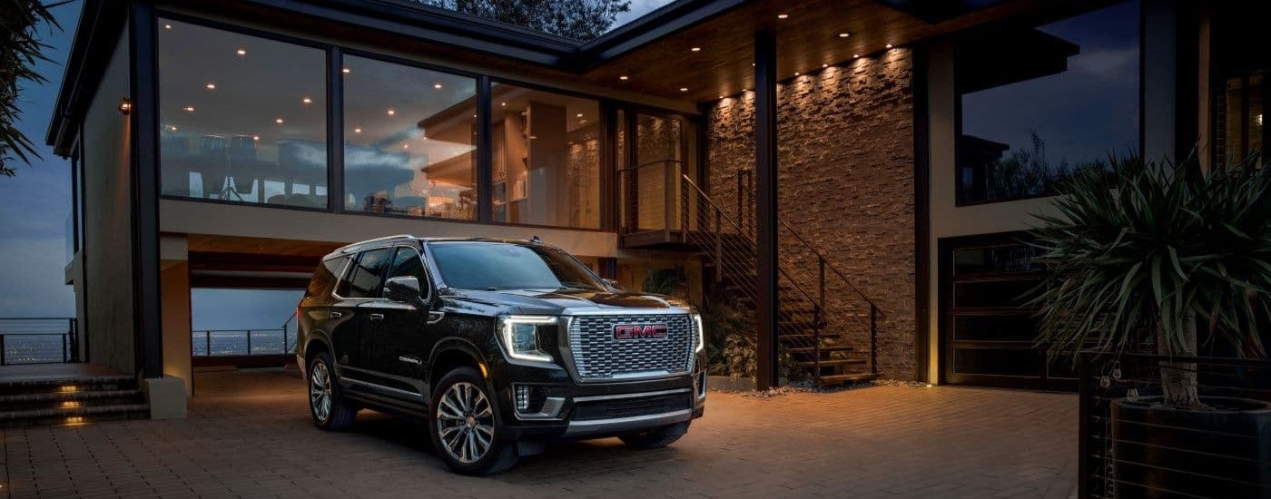 A black 2023 GMC Yukon Denali is shown parked on the driveway of a modern house.