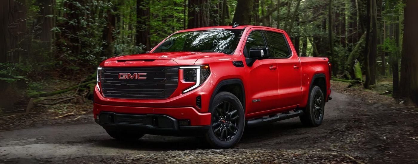 A red 2024 GMC Sierra 1500 Elevation angled left and parked off-road in a forest.